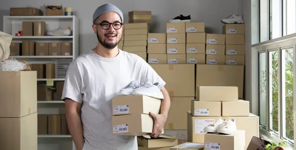 An online dropshipping small business owner standing in an e-commerce shipping warehouse with parcel boxes.